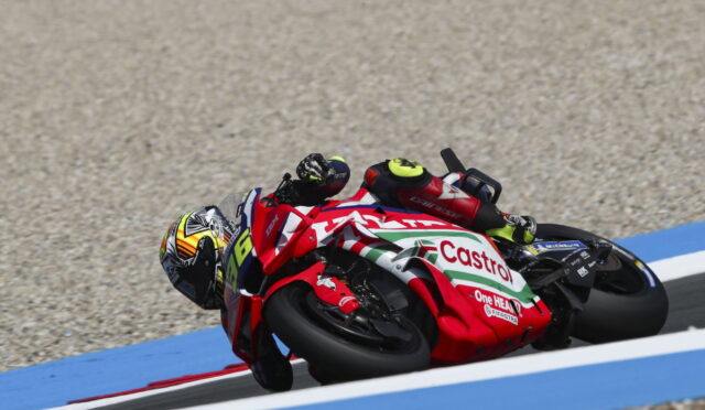 Motorcycle racer on a red-and-white Castrol bike leans into a sharp turn on a blue-curbed racetrack with gravel run-off nearby.