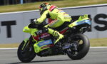 MotoGP rider in a neon-yellow suit leaning into a turn on a race track with a bright yellow bike.