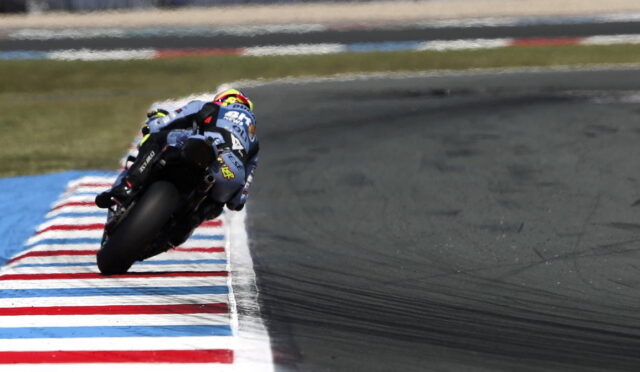 Motorcycle racer leans into a tight corner on a racetrack, riding along red-white-blue striped curbs.