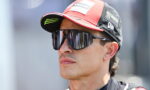 Man wearing a red and black Lenovo racing cap and mirrored sunglasses, looking to the right.