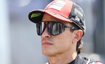 Man wearing a red and black Lenovo racing cap and mirrored sunglasses, looking to the right.