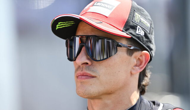 Man wearing a red and black Lenovo racing cap and mirrored sunglasses, looking to the right.
