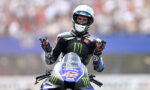 MotoGP rider in a black Monster Yamaha suit on a Yamaha bike, hands raised in celebration.