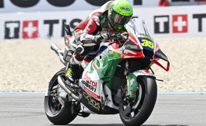 Motorcycle racer in a green helmet leans into a turn on a colorful race bike, number 35.
