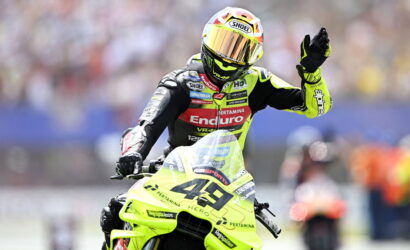 Motorcycle racer in a neon yellow suit on a lime-green bike, number 46, raising a gloved hand to the crowd.