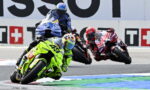 Four motorcycle racers lean into a turn; the lead bike is bright neon green with number 46, on a race track.
