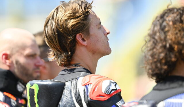 Male motorcycle racer in protective gear, side profile with eyes closed, at a track event; Monster Energy logo on shoulder pad visible
