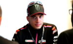 Male motorcycle racer wearing an Aprilia Racing jacket and a Monster Energy cap, during an interview.