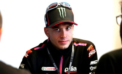Male motorcycle racer wearing an Aprilia Racing jacket and a Monster Energy cap, during an interview.