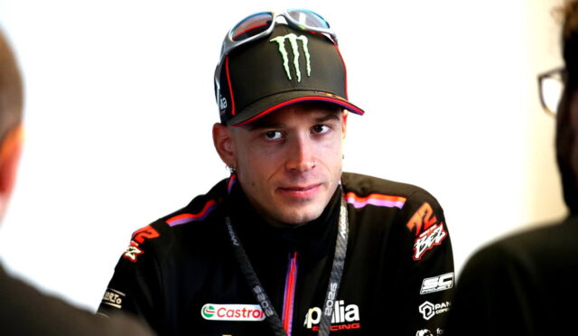 Male motorcycle racer wearing an Aprilia Racing jacket and a Monster Energy cap, during an interview.