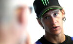 Young man wearing a black Monster cap leans in, talking to someone off camera.