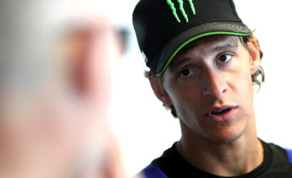Young man wearing a black Monster cap leans in, talking to someone off camera.