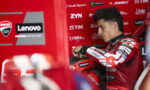 MotoGP rider in red Lenovo/Ducati suit sits in a red pit box, adjusting his glove.