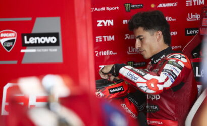 MotoGP rider in red Lenovo/Ducati suit sits in a red pit box, adjusting his glove.