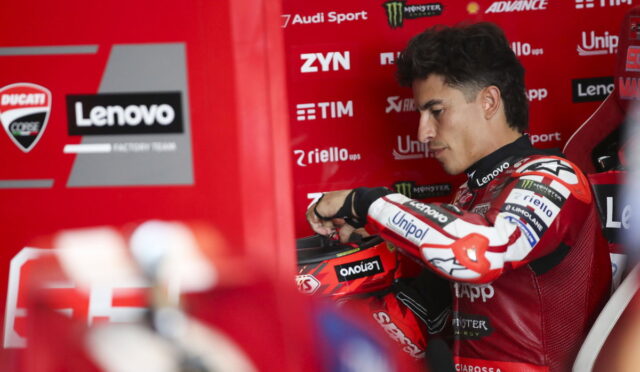 MotoGP rider in red Lenovo/Ducati suit sits in a red pit box, adjusting his glove.