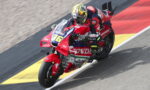 Motorcycle racer in a red Honda suit leans into a turn on a race track, bike #36 with sponsor decals visible.