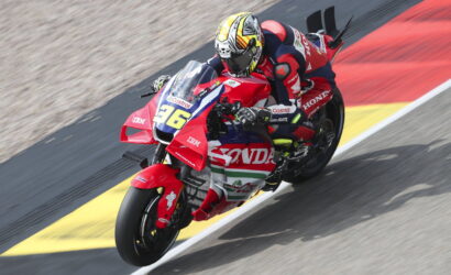 Motorcycle racer in a red Honda suit leans into a turn on a race track, bike #36 with sponsor decals visible.