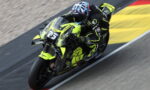 MotoGP rider leaning into a turn on a neon-yellow racing motorcycle on a race track.