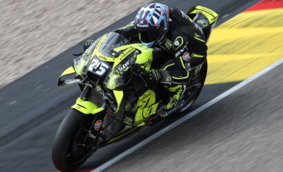 MotoGP rider leaning into a turn on a neon-yellow racing motorcycle on a race track.
