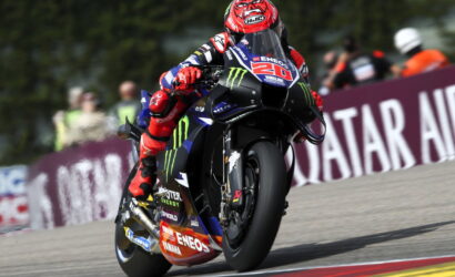 MotoGP rider #20 on a Yamaha race bike leans into a corner, sponsor decals visible on the bike and suit