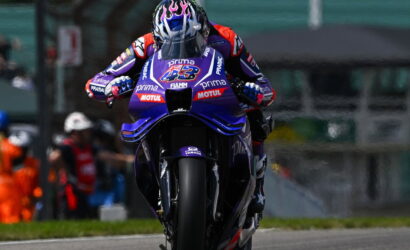 Professional motorcycle racer on a purple Yamaha bike speeding toward the camera on a racetrack, helmeted and in full race gear.