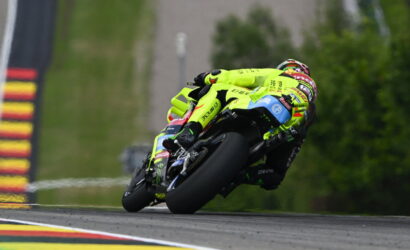 Moto racer in neon yellow suit leaning into a sharp turn on a race track, blue-and-black bike angled dramatically.