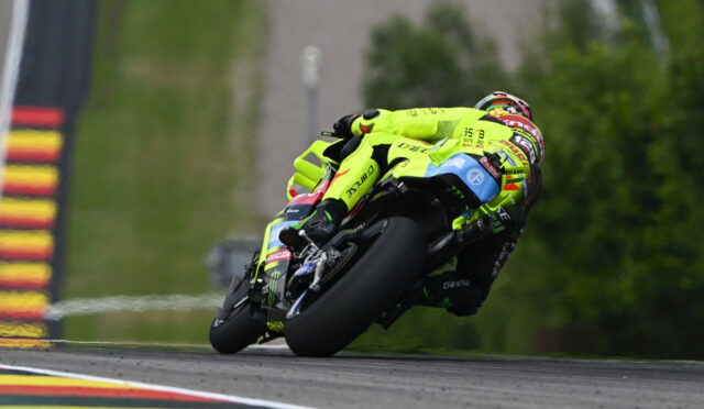 Moto racer in neon yellow suit leaning into a sharp turn on a race track, blue-and-black bike angled dramatically.