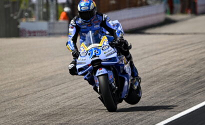 Motorcycle racer in blue riding suit leaning into a left-hand turn on a race track, number 73 visible on the blue bike.