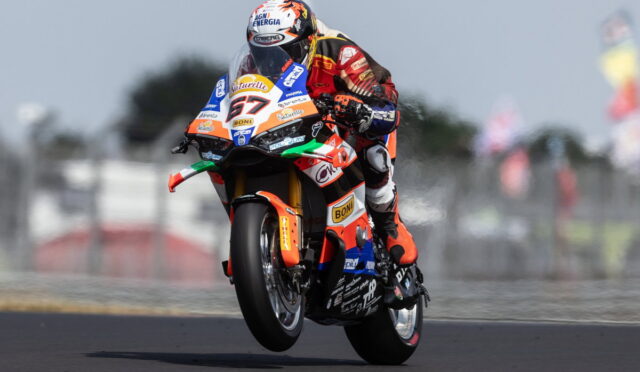 Moto racing rider on an orange, sponsor-labeled bike mid-air during a jump on track, number 67 visible on the front.