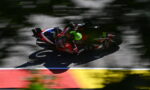 MotoGP rider in red and white gear with a neon green helmet leaning into a turn on a racetrack; motion-blurred background behind the bike.