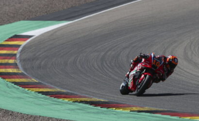 MotoGP rider in red gear leaning into a sharp curve on a race track with painted curbs.