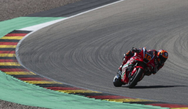 MotoGP rider in red gear leaning into a sharp curve on a race track with painted curbs.