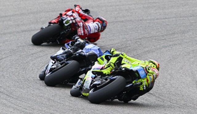 Three sportbike racers lean into a turn on a racetrack; foreground rider wears bright neon yellow gear on a neon-yellow bike with a blue bike behind and a red rider in the rearlust.