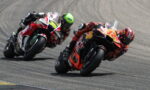 Two sport motorcycle racers lean into a left-hand turn on a race track, competing closely.