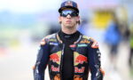 Moto racer in Red Bull KTM suit wearing sunglasses and cap, walking toward the pit area.