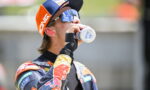 Motocross rider in orange-blue gear drinks water from a bottle during a break.