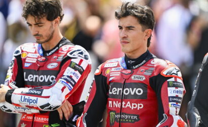 Two motorbike racers in red Lenovo suits stand side by side, looking serious and focused off-camera, with sponsor logos visible on their outfits.