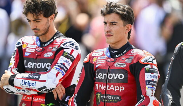 Two motorbike racers in red Lenovo suits stand side by side, looking serious and focused off-camera, with sponsor logos visible on their outfits.