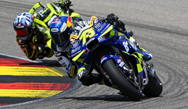 Two motorcycle racers lean into a right-hand curve on a race track; the lead rider rides a blue-yellow bike with number 73 and sponsor decals, closely followed by a neon yellow rider behind.