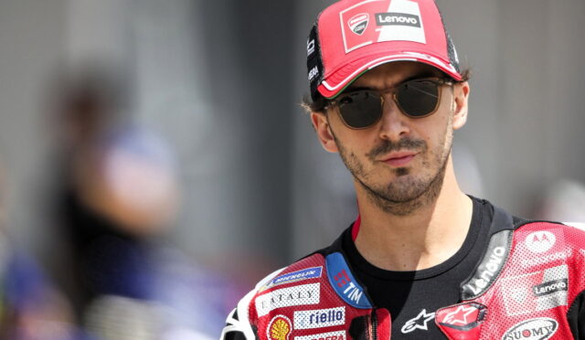Male motorcyclist in a red cap with sponsor logos and sunglasses, head-and-shoulders portrait in racing gear.