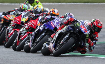 Group of motorcycle racers leaning into a tight turn on a race track in a close pack, tires screeching on asphalt.