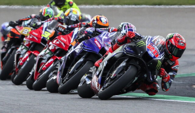 Group of motorcycle racers leaning into a tight turn on a race track in a close pack, tires screeching on asphalt.