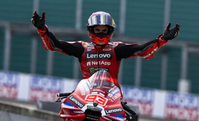 MotoGP rider in a red Lenovo racing suit raises arms in victory on the track