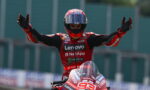 Moto racer in red suit raises arms in victory atop a red bike with number 93, Lenovo and NetApp sponsorships visible.