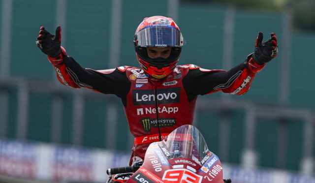 Moto racer in red suit raises arms in victory atop a red bike with number 93, Lenovo and NetApp sponsorships visible.