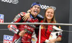 Two MotoGP riders celebrate on the podium with arms around each other, smiling for the camera.