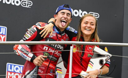 Two MotoGP riders celebrate on the podium with arms around each other, smiling for the camera.