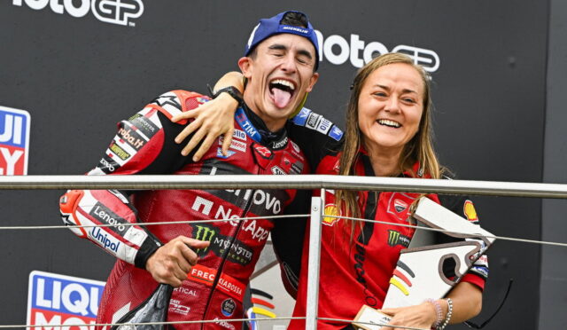 Two MotoGP riders celebrate on the podium with arms around each other, smiling for the camera.