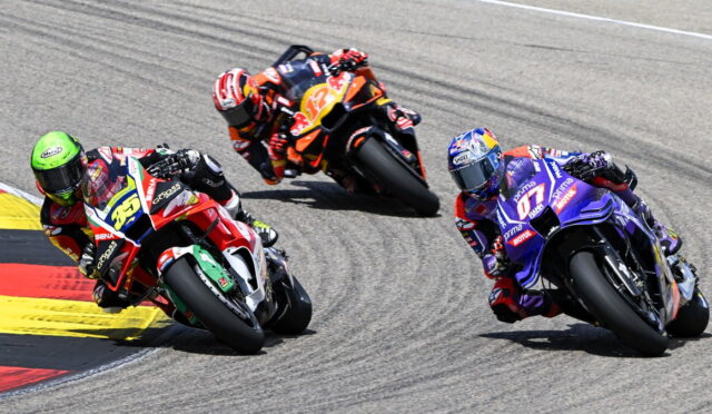 Three professional motorcycle racers lean into a sharp turn on a race track, colorful bikes close together.",