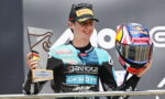 Moto rider on a podium holding a trophy in his left hand and a Red Bull helmet in his right.